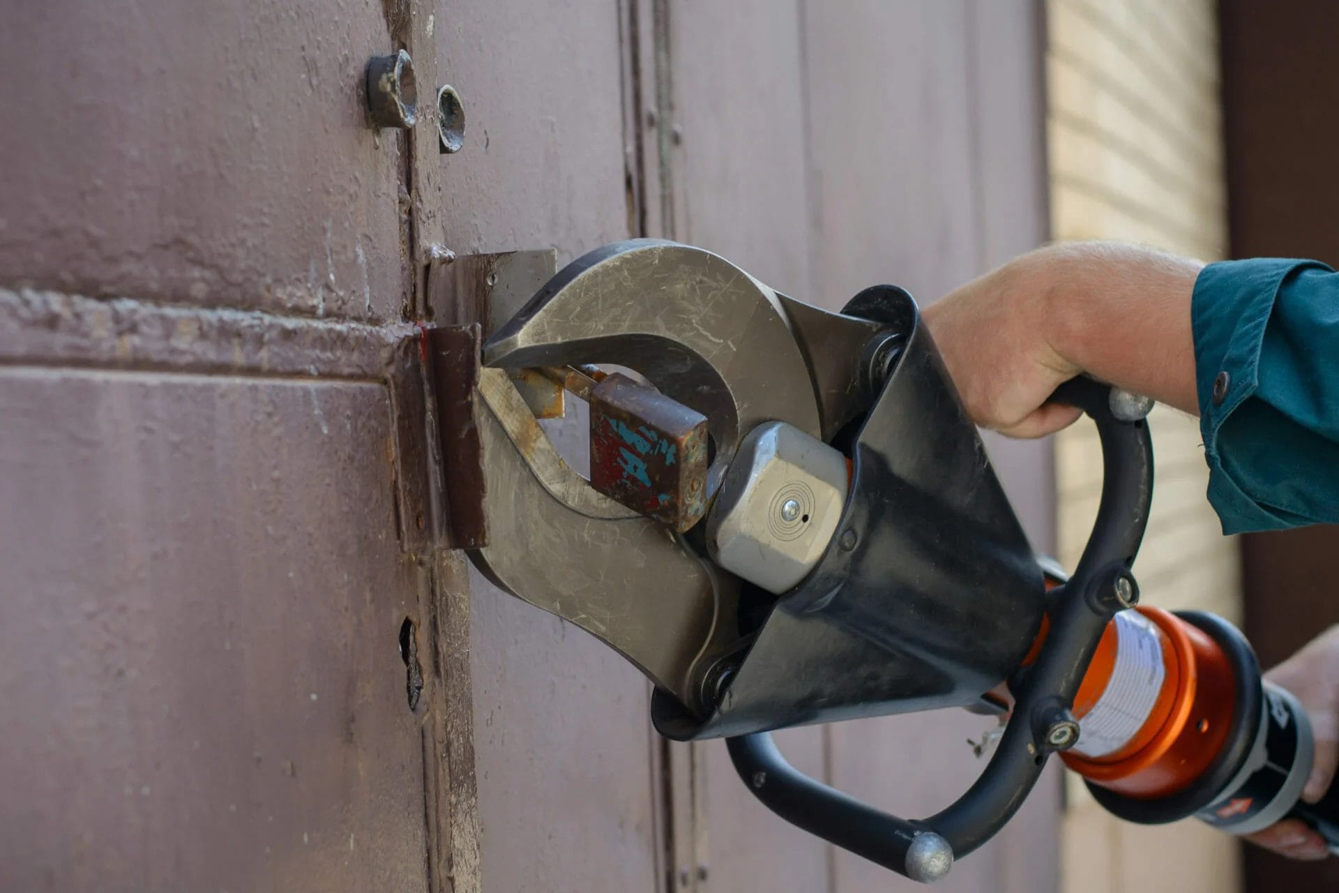An emergency locksmith using a pad lock cutter after a lost key cannot be found